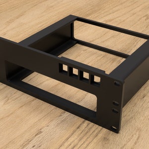 Puede incluir: Estante de metal negro con una abertura rectangular y varios agujeros pequeños en el lateral. El estante está diseñado para contener componentes electrónicos.