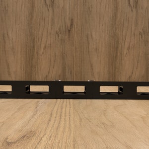 May include: Black metal rack with five rectangular openings. The rack is designed to hold and organize cables or wires.