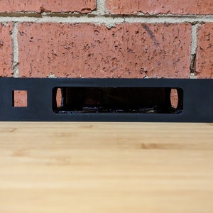 May include: Black metal rack with a rectangular opening, designed for mounting equipment. The rack has four holes on each side for mounting screws.