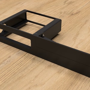 May include: Black metal rack with a sliding shelf and mounting brackets. The rack is designed to be mounted on a wall or other surface.