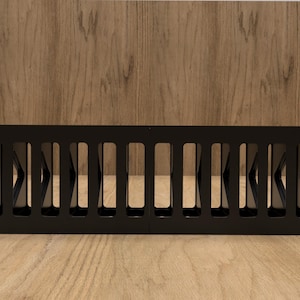 May include: A black metal cable management panel with rectangular and angled cutouts. The panel is designed to organise and route cables, and it has mounting holes on each end. The panel is shown against a wooden background.