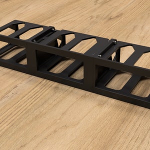 May include: Black metal rack with multiple slots for organizing cables or cords. The rack is designed to be mounted on a wall or surface.