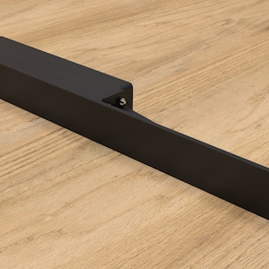 Peut inclure: Poignée de porte en métal noir avec un design long et rectangulaire. La poignée a un petit trou rond sur le côté gauche et une série de trous sur le côté droit.