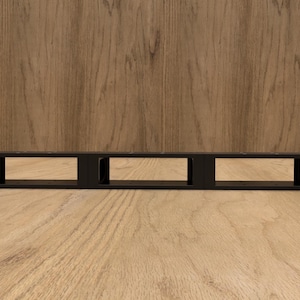 May include: A black, rectangular rack mount with three open sections. The rack mount is made of metal and has mounting holes on each end. The background is a light brown wood grain.
