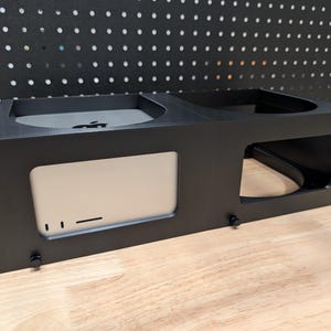 Può includere: Alloggiamento per montaggio su rack nero con più scomparti. L'alloggiamento ha un'apertura circolare, un'apertura rettangolare e una fessura rettangolare. Progettato per contenere dispositivi elettronici. Lo sfondo è una pannello forato nero.