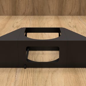 May include: A black metal rack mount component with a rectangular central opening and multiple mounting holes. The component has a trapezoidal shape on the sides and is designed for mounting electronic equipment. It sits on a wooden surface.