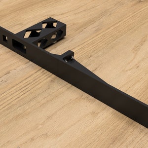 May include: Black metal bracket with a rectangular base and a vertical arm with a series of cutouts. The bracket is designed to be mounted to a wall or other surface.