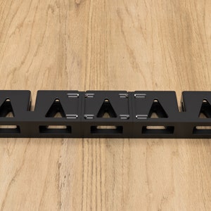May include: Black metal cable management rack with five compartments for organizing cables. The rack has a rectangular shape and is designed to be mounted on a wall or surface.