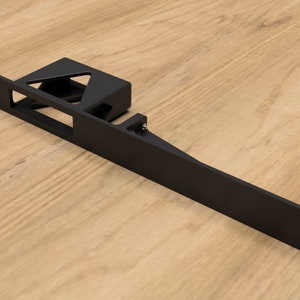 Puede incluir: Soporte de metal negro con un recorte rectangular y un recorte triangular más pequeño. El soporte tiene varios agujeros en los bordes.