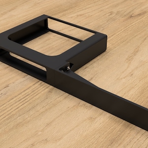 Puede incluir: Soporte de estante de metal negro con un brazo largo y recto que se extiende desde el lateral. El soporte tiene una abertura rectangular en el centro y está diseñado para soportar un estante.