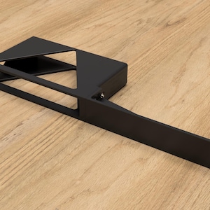 Op de afbeelding: Zwarte metalen plankensteun met een rechthoekige opening en een lange, platte arm die naar rechts uitstrekt. De steun is ontworpen om een plank of een ander object te dragen.
