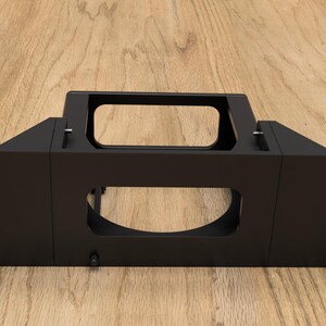 Puede incluir: Estante de metal negro con una abertura rectangular y una abertura ovalada más pequeña. El estante tiene cuatro agujeros a cada lado para montaje.