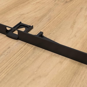 May include: Black metal bracket with a rectangular opening and a small, angled arm extending from the side. The bracket is designed to be mounted to a wall or other surface.