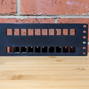 Peut inclure: Plaque murale en plastique noir avec 2 rangées de 10 trous rectangulaires, conçue pour le montage de câbles électriques ou de données.