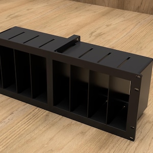 Puede incluir: Rejilla de ventilación de metal negro con forma rectangular y múltiples ranuras verticales. La rejilla de ventilación tiene un borde ligeramente elevado alrededor del perímetro.