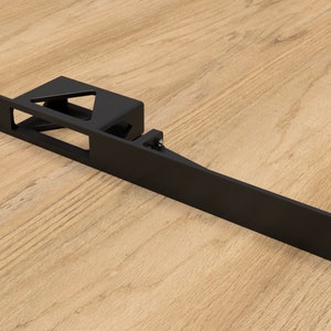 Puede incluir: Soporte de metal negro con una abertura rectangular y un recorte triangular. El soporte está diseñado para montarse en una pared u otra superficie.