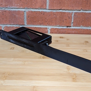 May include: Black metal bracket with a rectangular opening for a device. The bracket has a long arm extending to the right.