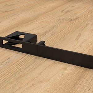 Può includere: Staffa da parete in metallo nero di forma rettangolare con un'apertura per un dispositivo. La staffa ha quattro fori di montaggio sul lato destro.