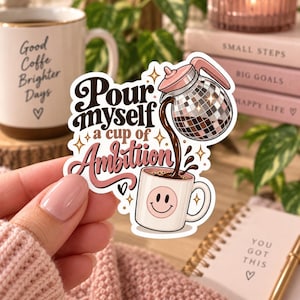 May include: A die-cut sticker featuring a disco ball coffee carafe pouring dark coffee into a light pink mug with a smiley face. The text reads "Pour myself a cup of Ambition" in dark brown and pink script. The design includes small star accents.