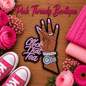 Op de afbeelding: Een geborduurde patch met een bruine hand met roze nagels, een zilveren ring, een kralenarmband en een zilveren horloge. De tekst "Clock That Tea" is in roze cursief geborduurd naast de hand, op een achtergrond met houtnerf.