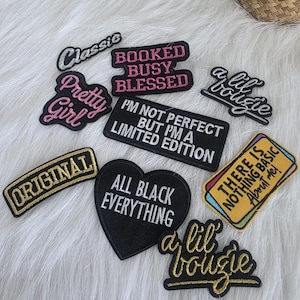 Pode incluir: Uma coleção de patches bordados com várias frases e designs. Os patches incluem textos como "Classic", "Pretty Girl", "Booked Busy Blessed" e "All Black Everything". As cores incluem preto, branco, rosa e dourado.