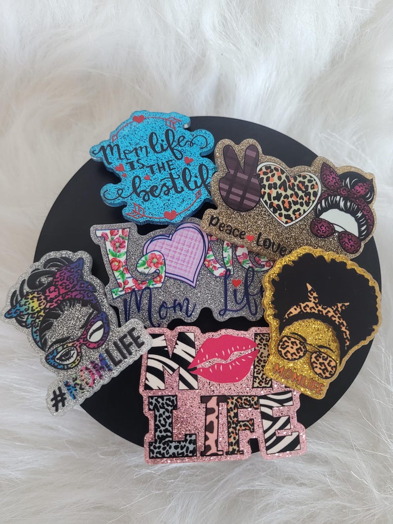 May include: A set of seven glitter iron-on patches with various designs, including a peace sign, a heart, a woman's face, and the words "Mom Life" and "#MomLife".