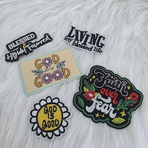Puede incluir: Un conjunto de parches bordados con frases inspiradoras. Los parches incluyen textos como "Blessed & Highly Favored", "Living my Blessed Life", "Good is Good" y "Faith over Fear". Los parches presentan diseños florales y de margaritas.