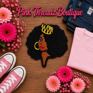 Puede incluir: Un parche bordado que muestra el perfil de una persona de piel oscura, cabello negro voluminoso, una corona amarilla y un pendiente de aro dorado. El texto Pink Threadz Boutique aparece arriba, rodeado de flores rosas, zapatillas rosas, una camiseta rosa claro y vaqueros azules.