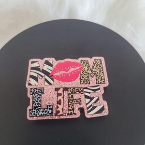 May include: Pink glitter "MOM LIFE" sign with a red lip print and animal print letters.