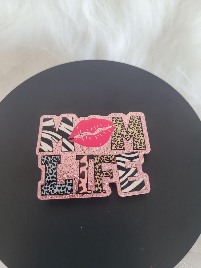 May include: Pink glitter "MOM LIFE" sign with a red lip print and animal print letters.
