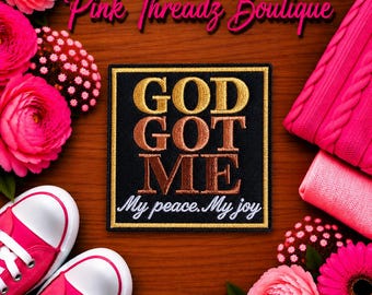 Op de afbeelding: Een vierkante geborduurde patch met een zwarte achtergrond en een gouden rand. De tekst luidt GOD GOT ME in gouden en koperkleurige blokletters, met daaronder My peace. My joy in wit cursief schrift. De patch is omringd door roze bloemen en sneakers.