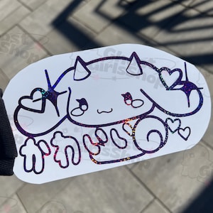 May include: A holographic sticker featuring a cartoon character with horns, large eyes, and a heart-shaped nose. The character is holding up two hands in a peace sign gesture. The sticker is on a white background and has a rainbow iridescent finish. The text "かわいい" is written in Japanese below the character.
