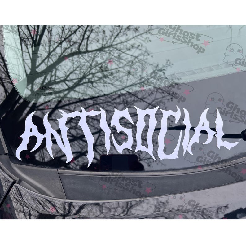 May include: White vinyl decal with the word "ANTISOCIAL" in a gothic font. The decal is displayed on a car window, with a blurred background of tree branches and a cloudy sky.