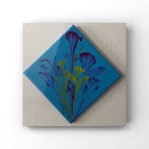May include: A blue canvas painting with a floral design. The flowers are purple, yellow, and green. The painting is on a white background.