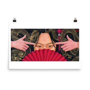 May include: A woman with dark hair partially covers her face with a red folding fan.  She is framed by a black background with a gold dragon design.  The woman is pointing her fingers at the viewer.