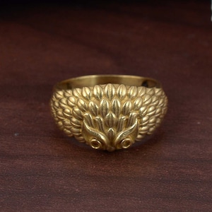 May include: A gold ring with a detailed hedgehog design. The hedgehog's face is prominent, with two small eyes.