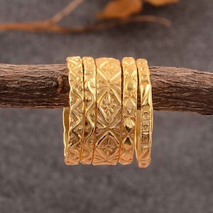 Puede incluir: Un conjunto de seis anillos apilables de color dorado con intrincados patrones geométricos. Los anillos están dispuestos en una rama de madera marrón.