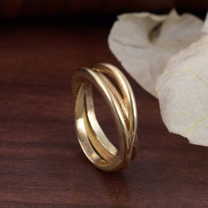 May include: A gold-toned ring with a unique, interwoven design. The ring is made of two bands that are twisted together to create a three-dimensional effect.