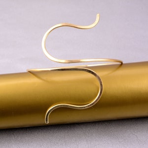 May include: A gold-toned metal bracelet with a unique, wavy design. The bracelet is open and flexible, making it easy to put on and take off.