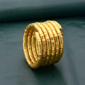 May include: A gold-colored bracelet made of multiple coiled bands of linked, cylindrical beads.