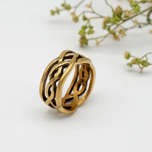 Puede incluir: Un anillo dorado con un diseño trenzado. El anillo está hecho de metal y tiene un acabado liso.