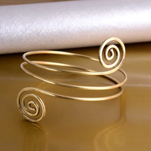 May include: A gold-toned metal bracelet with a double-spiral design. The bracelet is made of thin wire and has a simple, elegant look.