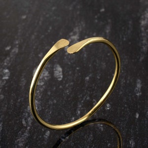 May include: A simple gold bangle bracelet with a unique open design. The bracelet is made from a single piece of metal that is bent into a circle and then has a small gap cut out of it. The gap is designed to allow the bracelet to be easily slipped on and off the wrist.