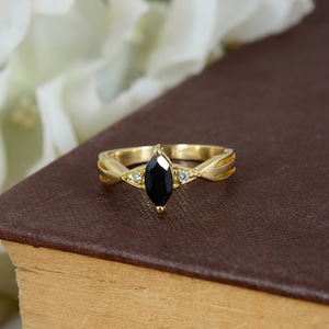 May include: A gold ring featuring a black marquise-shaped gemstone and two smaller clear gemstones on the band.