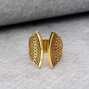 May include: A gold-toned ring with a geometric design. The ring is open in the back and has a triangular shape.