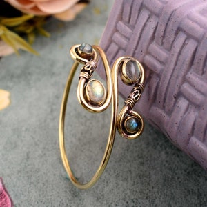 May include: A gold-toned bracelet with a swirling design and three iridescent gemstones. The bracelet is made of wire and has a delicate, feminine look.