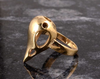 Puede incluir: Un anillo de color dorado con un diseño único que presenta una cabeza de pájaro ahuecada. El anillo está hecho de metal y tiene un acabado liso y pulido.