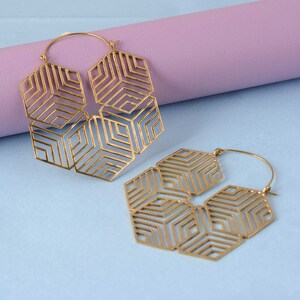 May include: A pair of gold hoop earrings with a geometric design. The earrings are made of metal and have a delicate, intricate pattern.