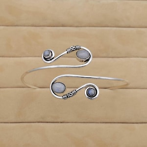 May include: Silver cuff bracelet with a delicate, curved design and three oval moonstone accents.