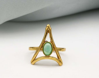 May include: A gold ring with a geometric design featuring a green oval gemstone in the center.